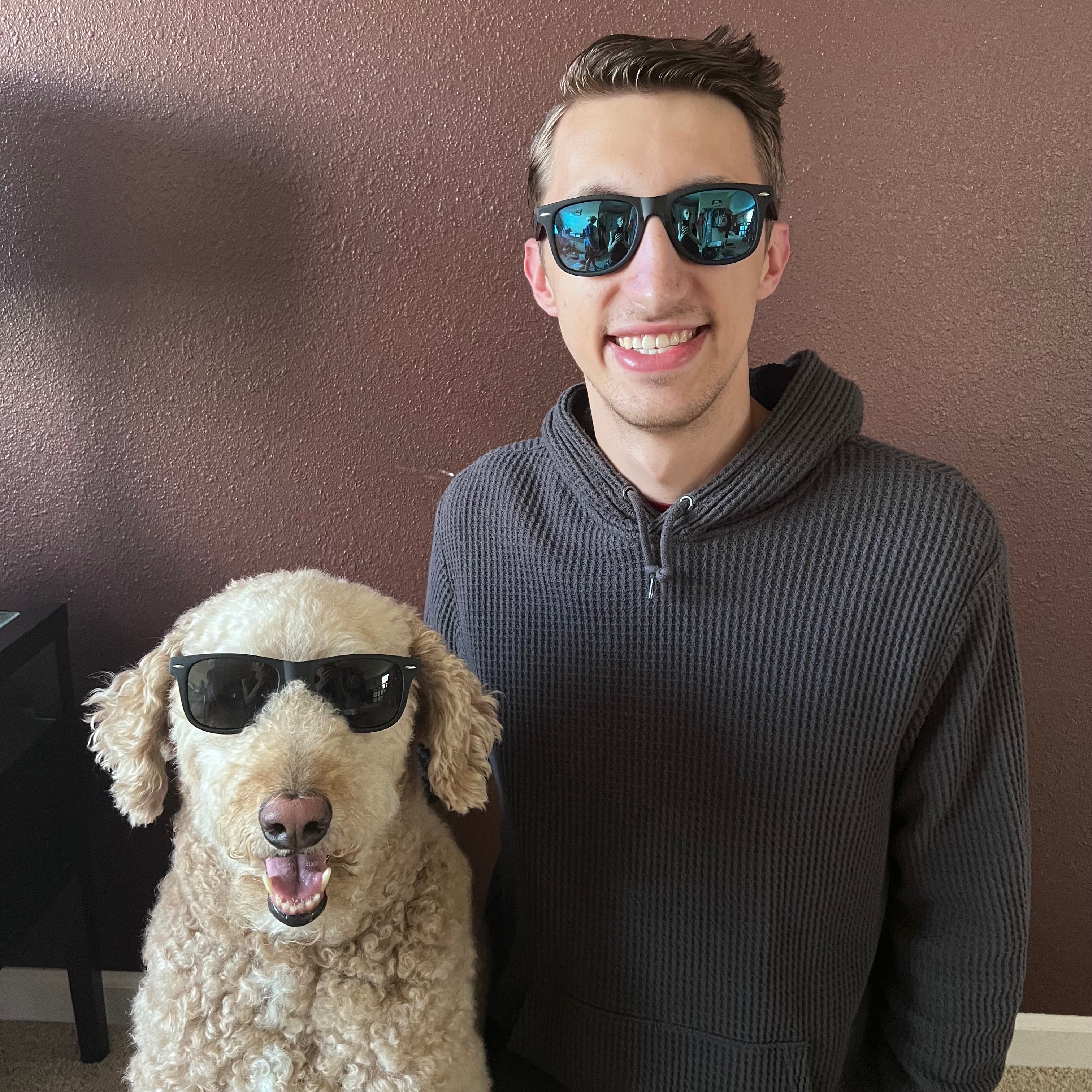photo of a young man with brown hair and a tan-colored fluffy dog, both wearing sunglasses